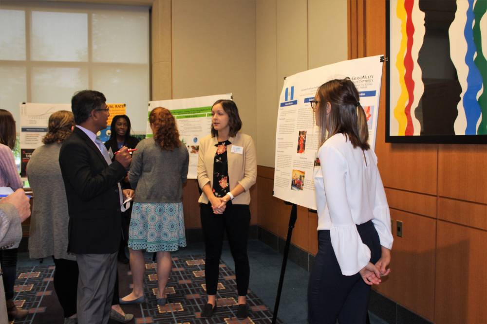A group of attendees standing around another poster presentation, asking questions
